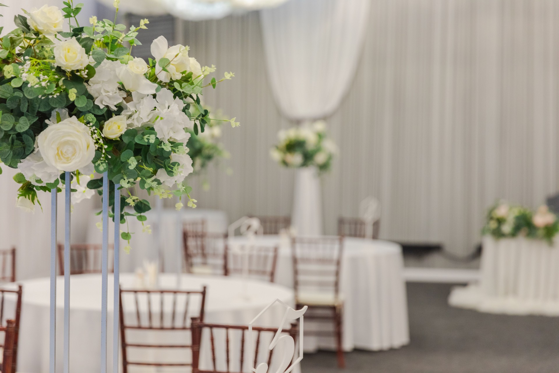 Decorated interior for festive event. Fancy table set for dinner with white flower composition in restaurant, luxury interior background. Wedding elegant banquet decoration arranged by catering service.